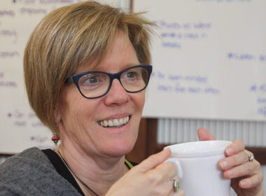 Women smiling over a cup of tea with whitebaord in the background